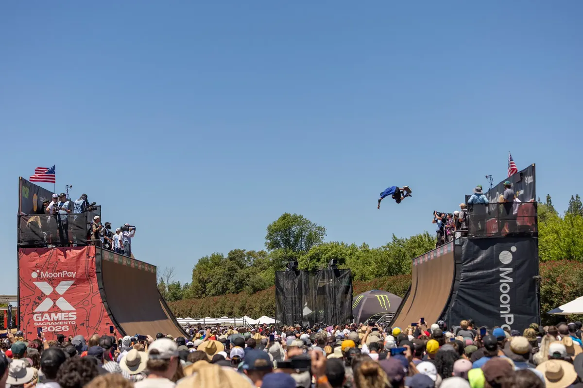 A skateboarder launches off a ramp in mid-air during a vibrant X Games event.