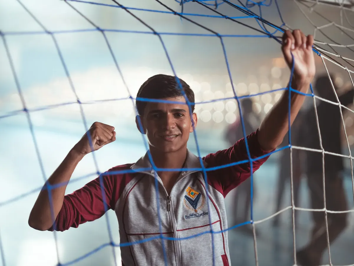 Young male celebrating inside a soccer net, showcasing sports enthusiasm in an indoor setting.