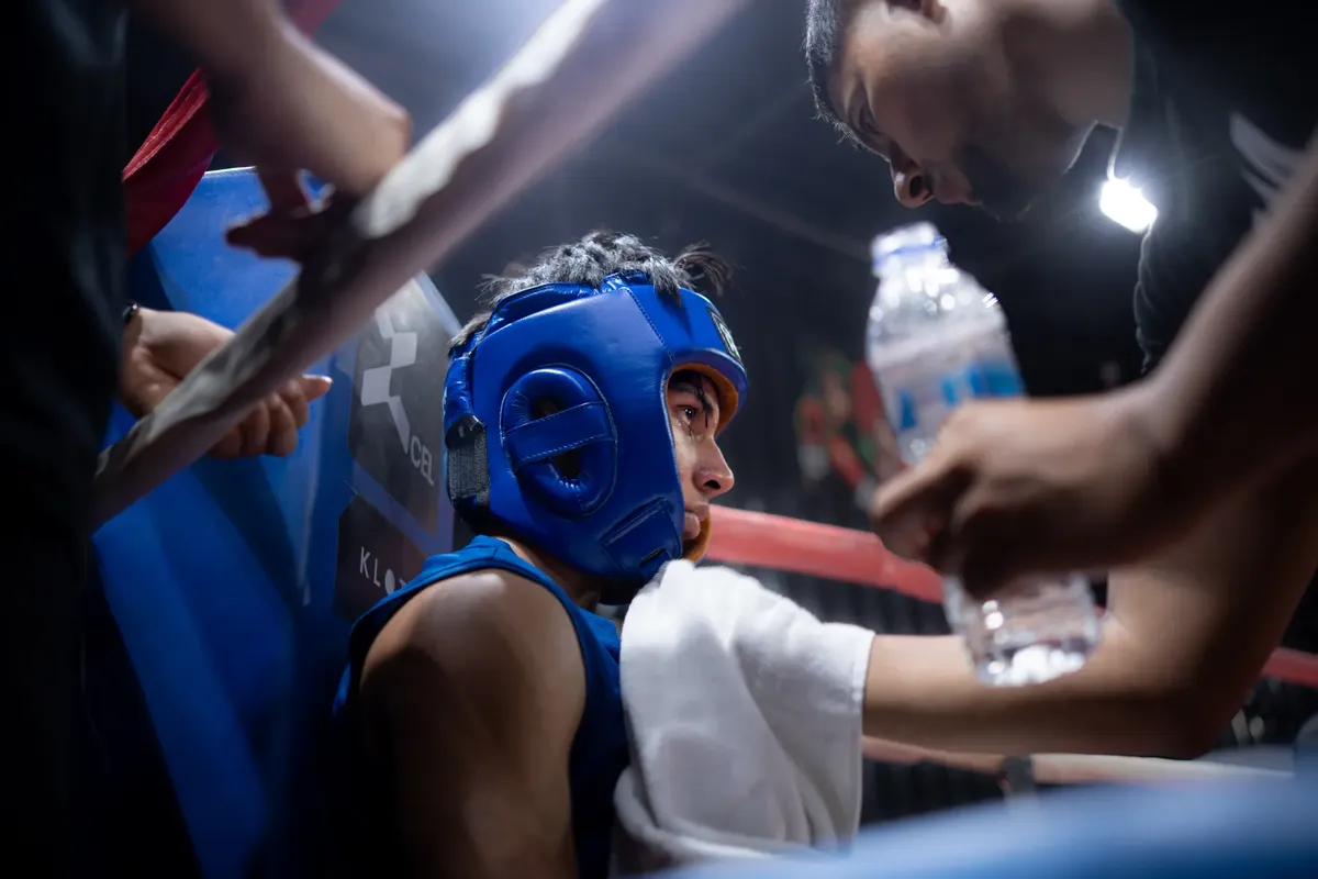 Boxer wearing blue helmet resting between rounds, listening to coach inside boxing ring.
