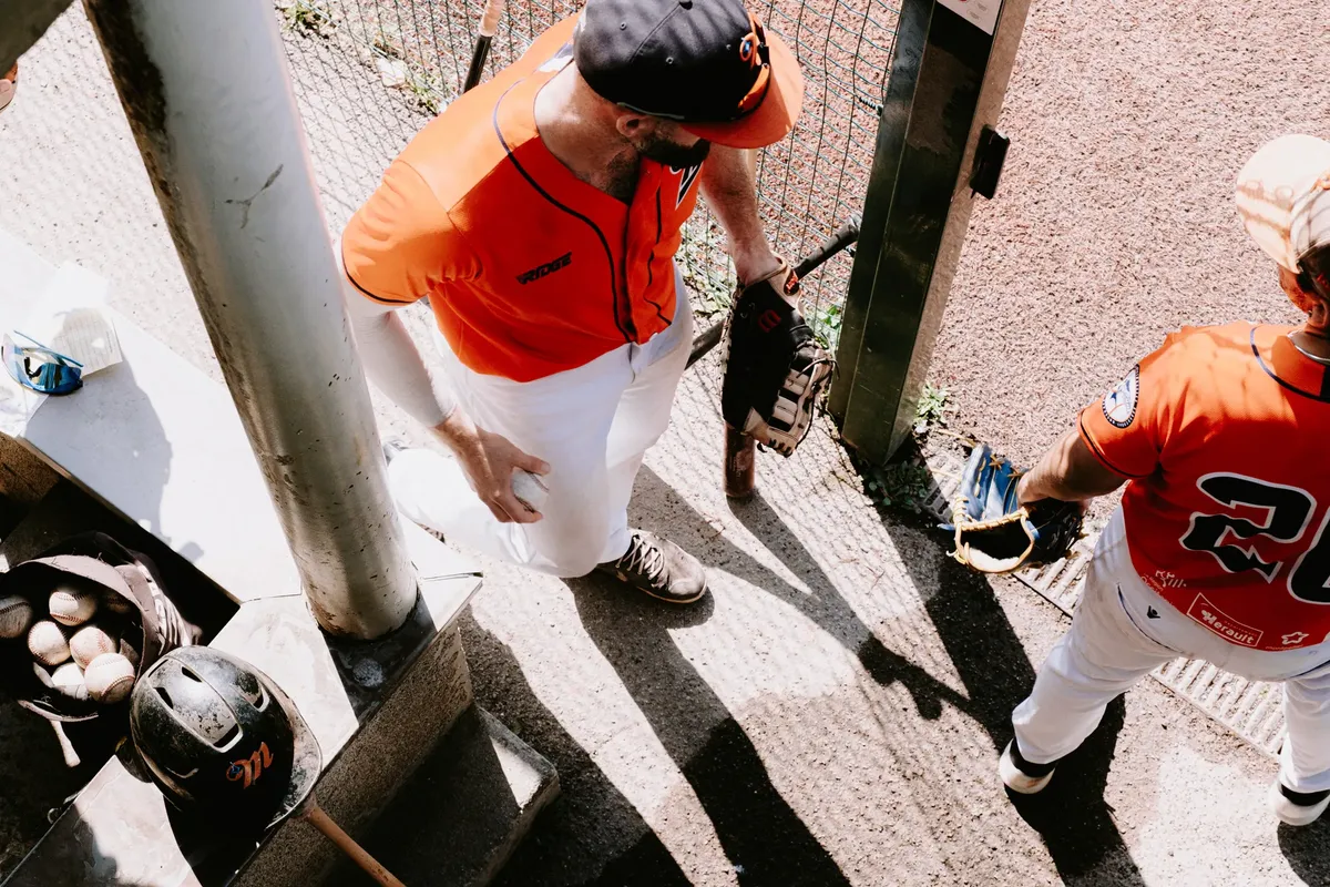 Overhead shot of two baseball players in a dugout wearing orange uniforms, ready for the game.