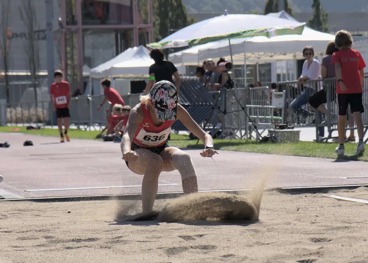 Female athlete captured mid-landing in the long jump event during a sunny sports meet.