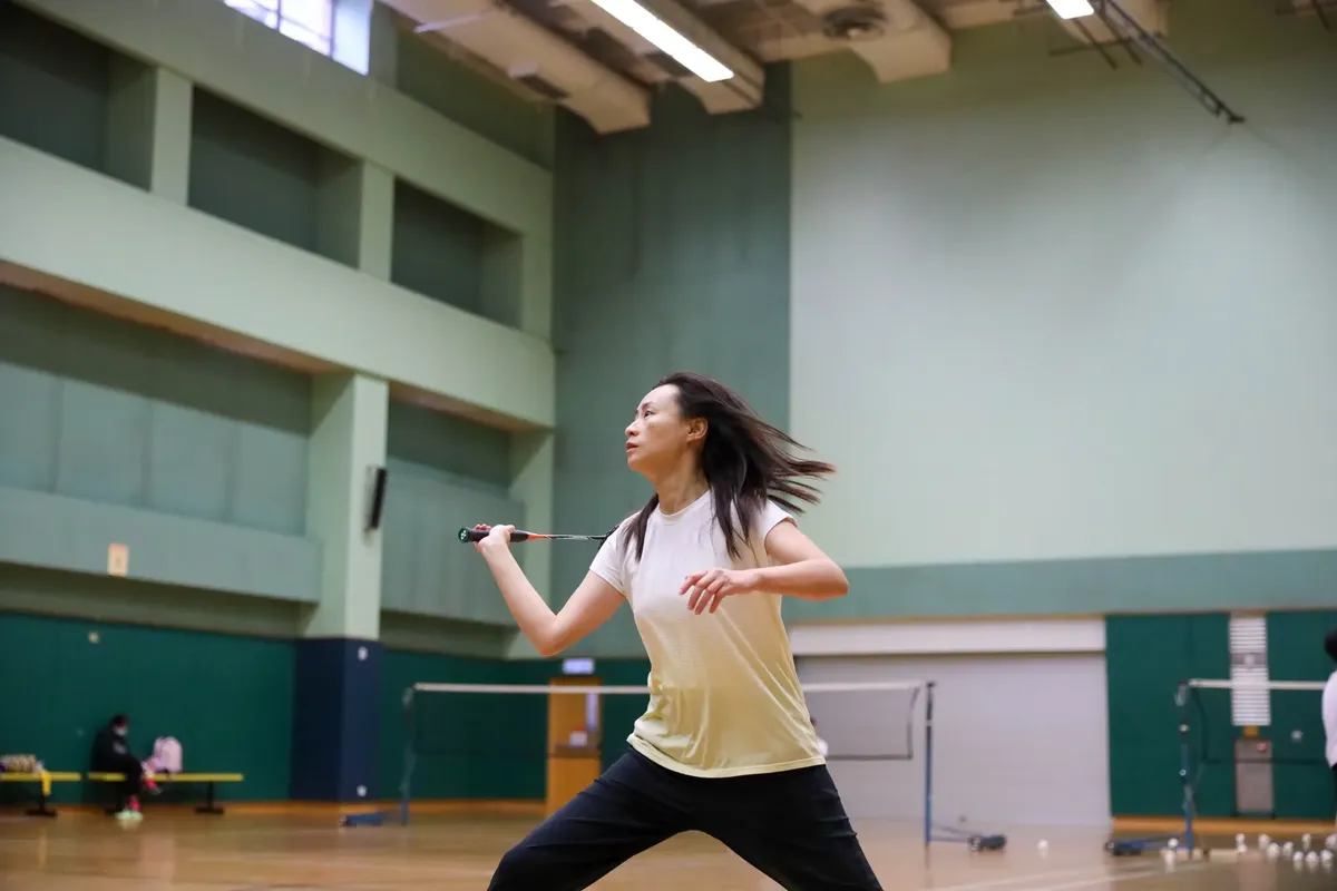 室內體育館中一名女子進行羽毛球運動的動態動作照片。