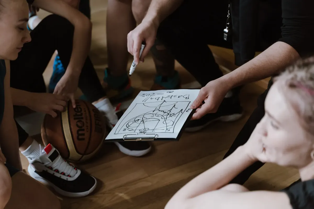 Close-up of a basketball team huddling with the coach discussing strategy indoors.