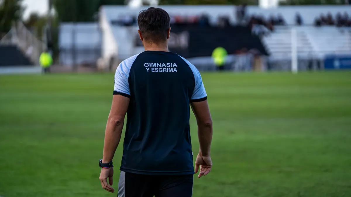 Back view of soccer coach at Gimnasia y Esgrima stadium during a match.
