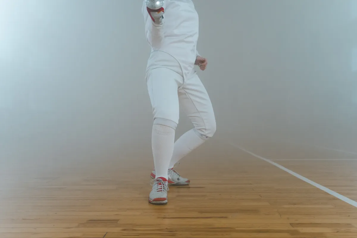 Fencing athlete executing a lunge with epee in indoor sports arena.